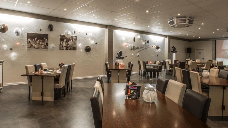 Een modern restaurant met lichte tafels en stoelen. De muren zijn gedecoreerd en het licht is zacht.