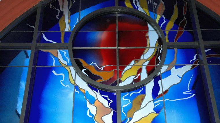 Une fenêtre en verre colorée et moderne avec un grand cercle rouge au centre.
Entourée de lignes entrelacées en bleu, blanc et jaune.