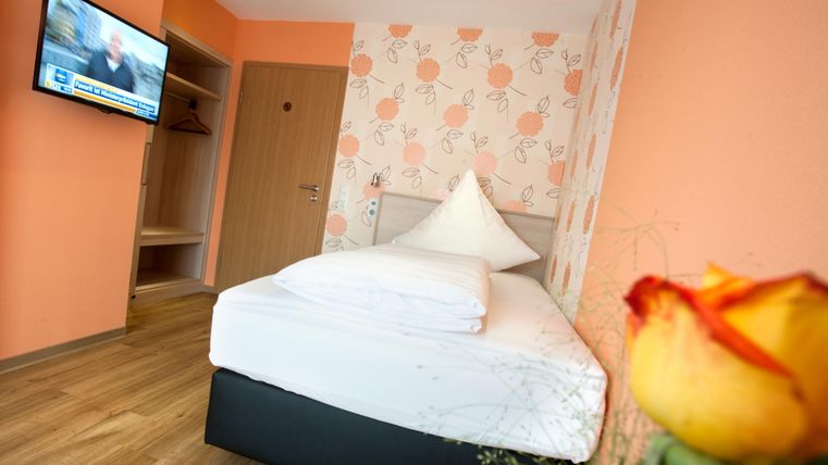 A cozy room with a single bed and modern amenities. There is a television on the wall and the walls are friendly in an orange tone.