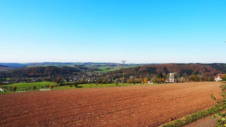 A wide landscape with a field in the foreground and gentle hills in the background. The sky is clear and blue, ideal for a sunny day.