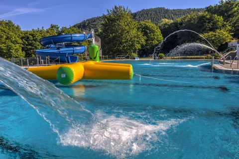 Ein Spaßbad mit Rutschen und großen Wasserflächen. Die Blau- und Grüntöne schaffen eine erfrischende Atmosphäre.