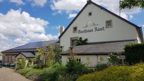 Ein gemütliches Gasthaus mit Blumenbeeten und moderner Solaranlage. Der Himmel ist klar mit einigen Wolken.