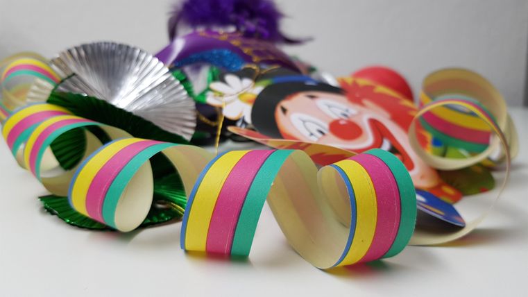 Bunte Luftschlangen und eine Clownmaske liegen auf einem Tisch. Die fröhlichen Farben bringen eine festliche Stimmung.