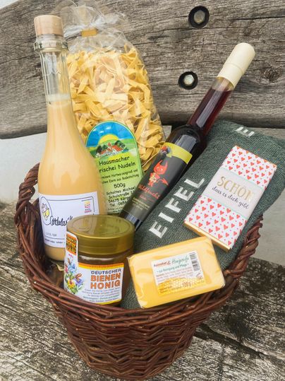 Ein Geschenkkorb mit verschiedenen lokalen Produkten, darunter Nudeln, Honig, Sirup und ein Handtuch. Die Artikel sind in einem hübschen korb angeordnet und bieten eine Vielzahl von Köstlichkeiten.