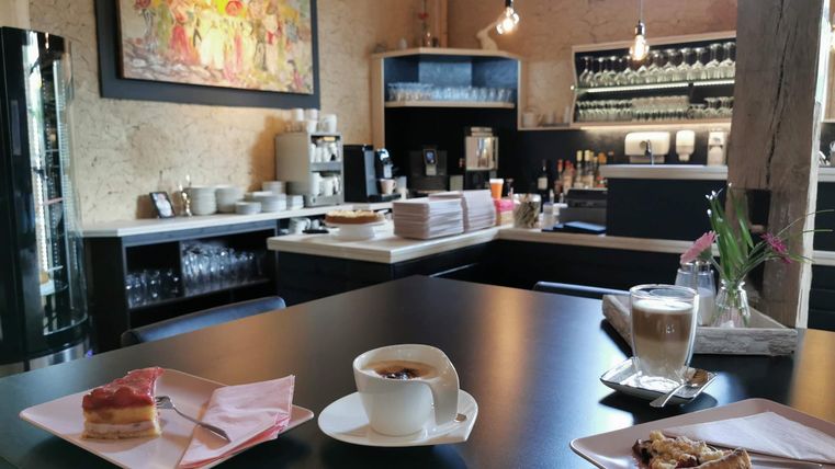 A cozy cafe corner with a modern bar area. Coffee and cake are on the table, surrounded by a warm atmosphere.