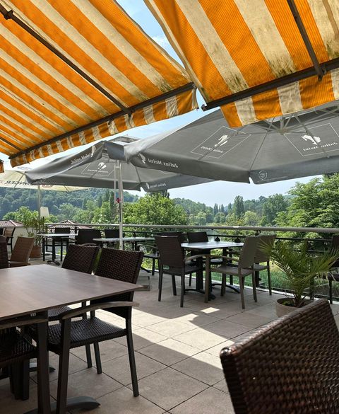 Een gezellige buitenruimte van een café met tafels en stoelen. De terrassozonweringen in oranje en wit bieden bescherming tegen de zon.
