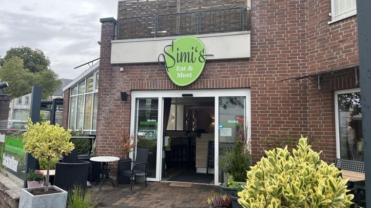 Een gezellig restaurant met de naam "Simi's Eat & Meet". De ingang is omgeven door planten en zitplaatsen.
