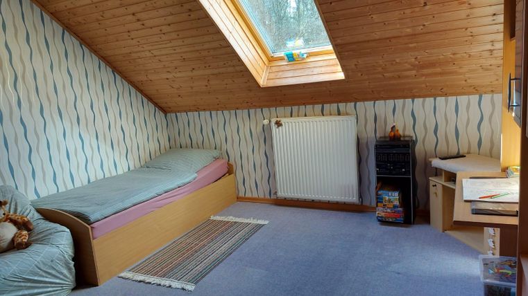A cozy attic room with a single bed and a desk. The room has a sloping roof and a window that lets in plenty of light.