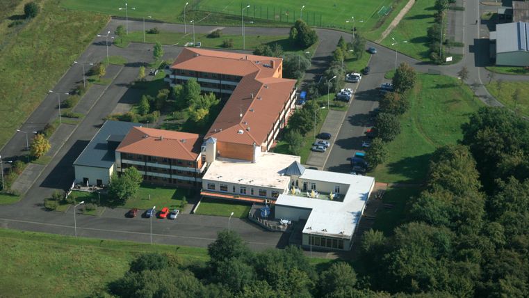 An overview of a modern building with red roofs and parking lots.
Surrounded by green spaces and a sports field.