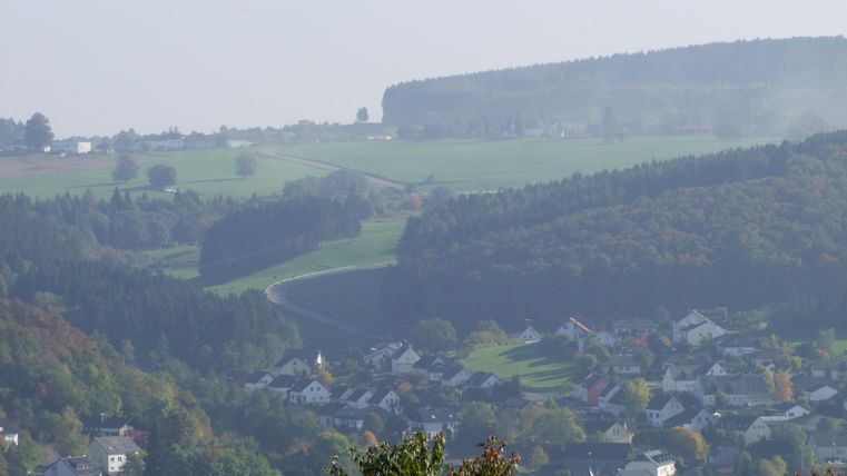 A picturesque landscape with gentle hills and a small village in the foreground. The surroundings are green and wooded, ideal for nature lovers.