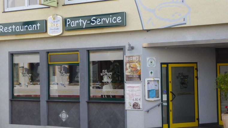 Un restaurant avec une façade simple et un service de traiteur. Les fenêtres dégagent une atmosphère conviviale et la porte d'entrée est bien visible.