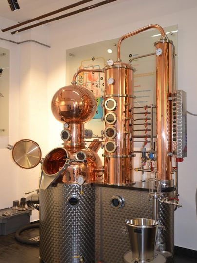 A modern distillery made of copper and stainless steel. It is located in a well-lit room and showcases various technical elements.