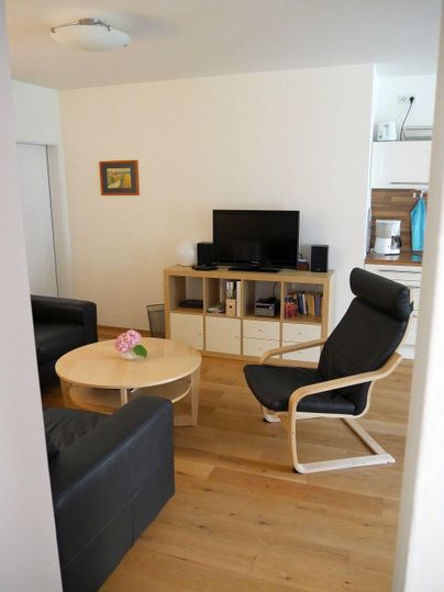 A modern living room with a black sofa and a comfortable chair. The room is bright and inviting, with a table and a television.
