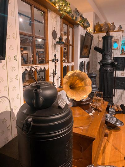 A traditional room with antiques, including a black kettle and a gramophone. The walls are decorated with floral patterns and there are wooden objects in the room.