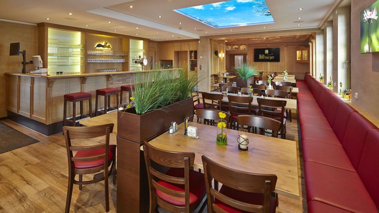 A modern restaurant with wooden tables and red benches. Ceiling lights create a pleasant atmosphere.