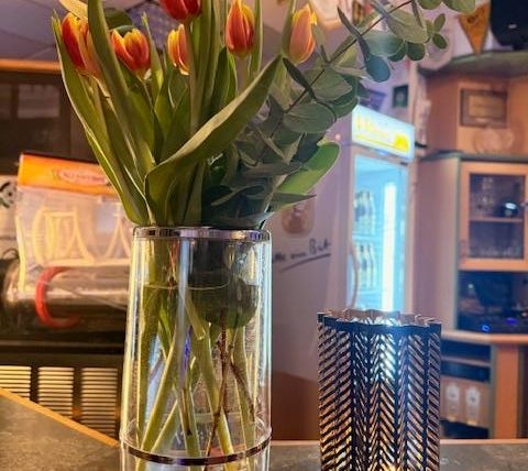 A glass vase with colorful tulips and eucalyptus is on a table. Next to it is an elegant candle holder.