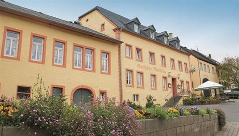 An elegant yellow building with several windows and a canopy. There are flower beds and a small square in the foreground.