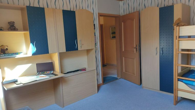 A bright, child-friendly room with a bunk bed and a desk. The walls are decorated with a blue and white pattern.