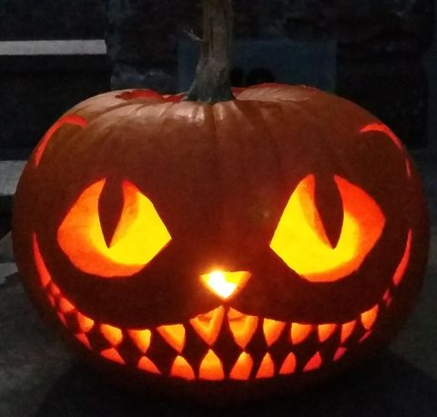 A glowing Halloween pumpkin with a grinning face and sharp teeth. The eyes are large and expressive, creating a creepy atmosphere.