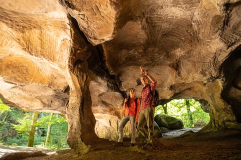 Zwei Wanderer stehen in einer Felsenhöhle mit gewölbter Decke und schauen nach oben.