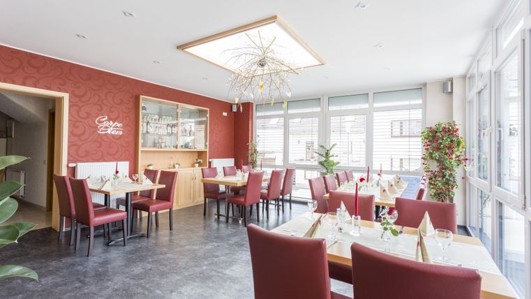 A modern restaurant with red-gray walls and elegant tables. Large windows provide plenty of daylight and create an inviting atmosphere.