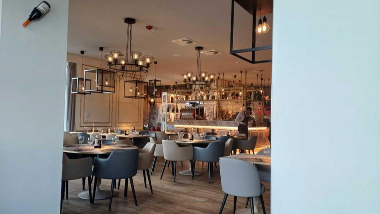 Een modern restaurant met elegante tafels en stoelen. De sfeer is gezellig, met stijlvolle verlichting en een open keuken.