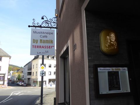 A sign for a music pub and café named "by Namik" is attached to the wall.
It is a quiet street with several buildings in the background.