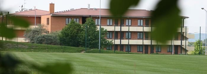 A modern building with several floors stands in a green landscape. The sky is clear and the surroundings are quiet.
