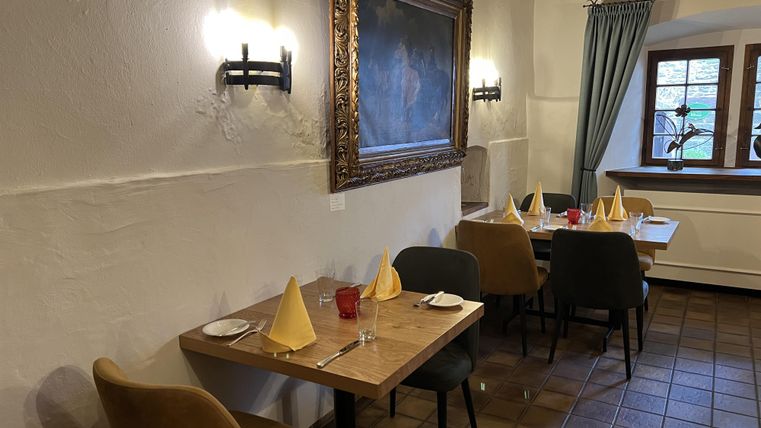 Een gezellig restaurant met houten tafels en elegante tafelkleedjes. Aan de muur hangt een groot schilderij, en door het raam valt zacht licht.