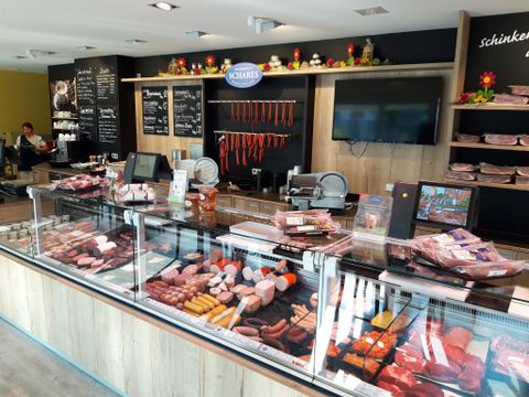 Une boucherie avec un large choix de saucisses et de viandes en vitrines. À l'arrière-plan, d'autres produits et la surface de vente sont visibles.