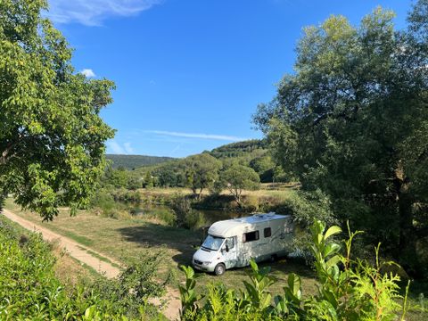 Ein Wohnmobil steht in einer ruhigen, grünen Landschaft. Im Hintergrund sind Bäume und ein blauer Himmel zu sehen.