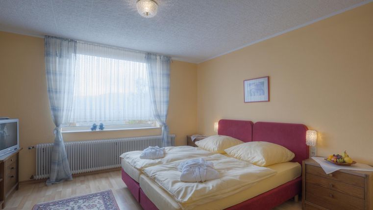 Ein gemütliches Schlafzimmer mit zwei Betten, hellen Wänden und einem großen Fenster. Ein Fernseher und ein Nachttisch ergänzen die Einrichtung.