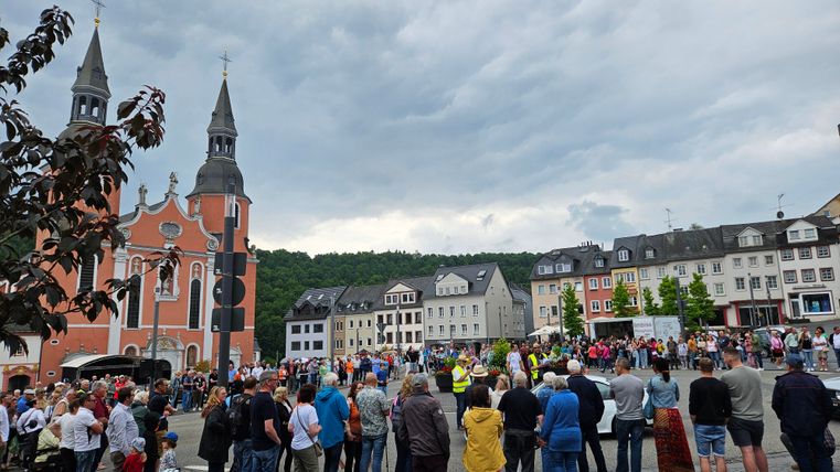 A lively square with a church in the background and many people. The sky is cloudy and the atmosphere seems festive.