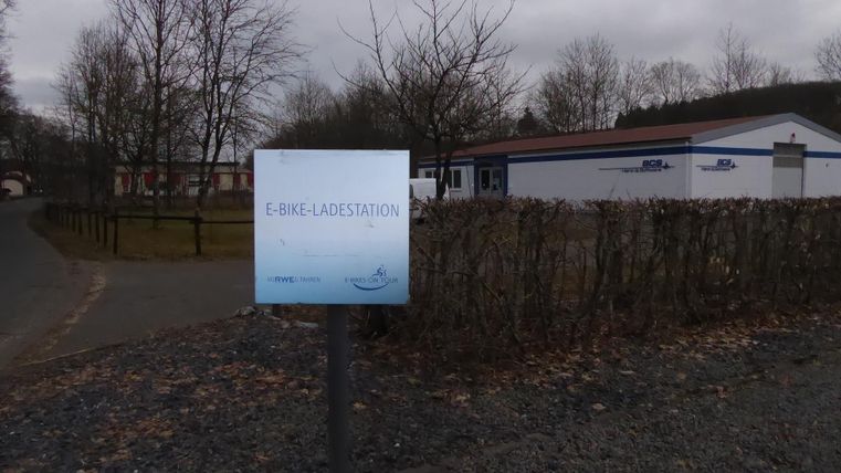An e-bike charging station is clearly visible. In the background, there is a building with a gray facade and bare trees.