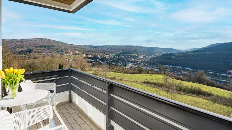 Ein Balkon mit einem Tisch und Stühlen, umgeben von einer schönen Landschaft. Im Hintergrund sind Hügel und ein blauer Himmel zu sehen.
