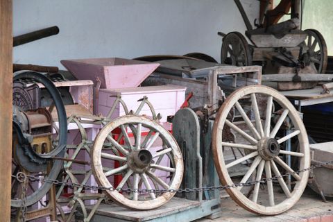 A collection of old agricultural machinery and wooden wheels in a storage room. The equipment is arranged in various colors and shapes.