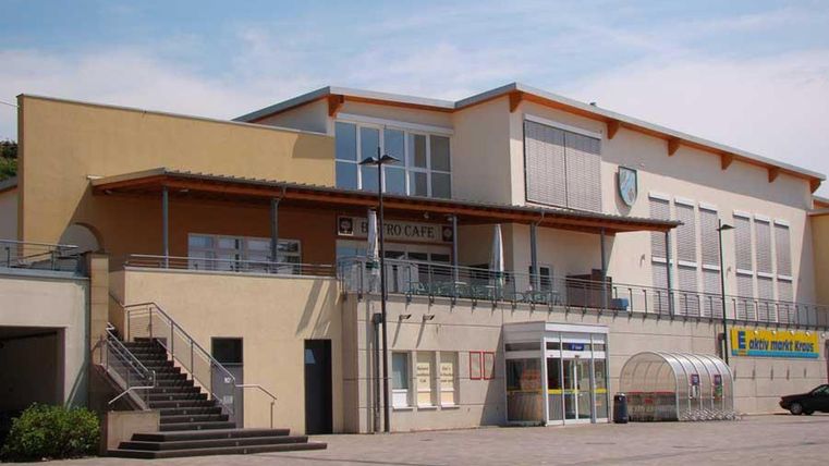 Een modern gebouw met een groot terras en een entree. Voor het gebouw zijn treden en een geplaveide ruimte.