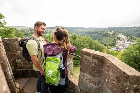 Ein Paar steht auf einem Aussichtspunkt und genießt die Aussicht auf das grüne Tal. Sie tragen Rucksäcke und scheinen glücklich und entspannt zu sein.