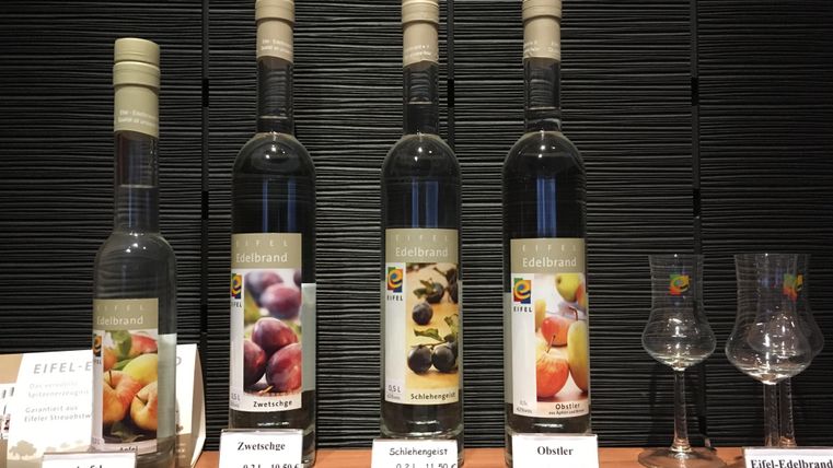 Four bottles of various fruit brandies are presented on a table. Next to the bottles are two glasses and price tags for the products.