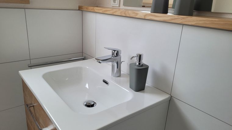 A modern bathroom with a white sink and an elegant faucet. Decorative gray containers are on the shelf.