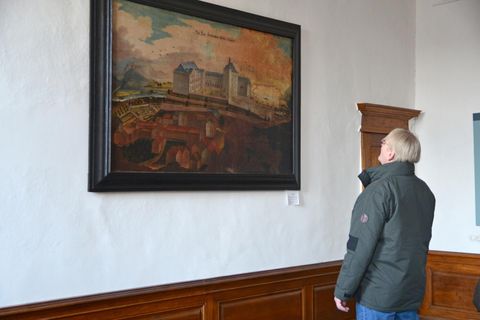 Une personne regarde une peinture sur le mur. L'image montre un paysage impressionnant avec des bâtiments historiques.