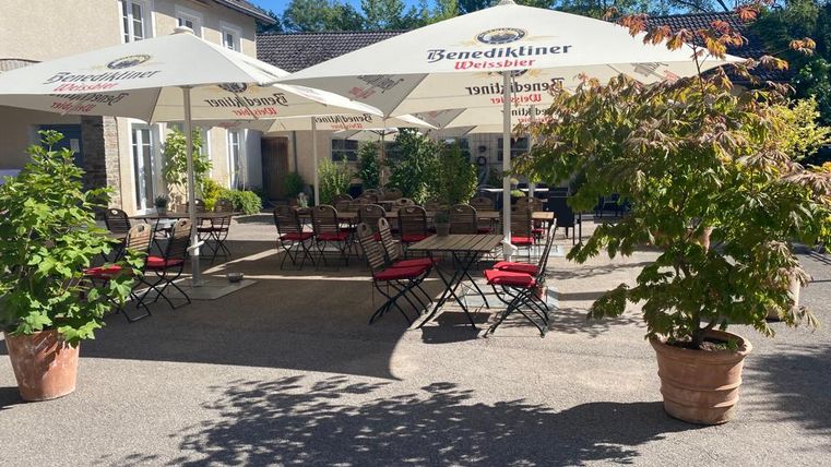 Une terrasse confortable avec des chaises et des tables noires sous des parasols. Entouré de plantes vertes et d'arbres, l'endroit offre une ambiance accueillante.