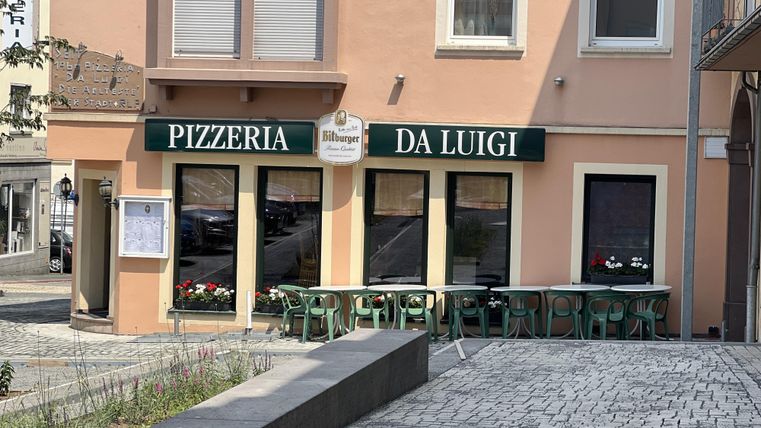 Une pizzeria nommée "Da Luigi" dans un bâtiment lumineux. Dehors, il y a des chaises et des tables vertes dans un environnement calme.