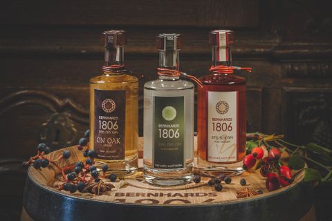 Three bottles of spirits are standing on a wooden barrel. Each bottle has a different label and is surrounded by decorative natural materials.