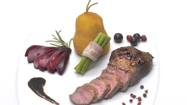 A stylishly arranged plate with beef steak, a baked pear, asparagus, and red beet. Accompanied by some berries and a fine sauce.