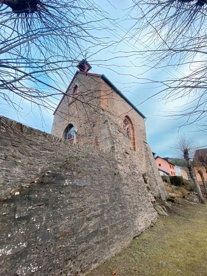 A historic church stands near a stone wall. The sky is cloudy and the surroundings feel quiet.
