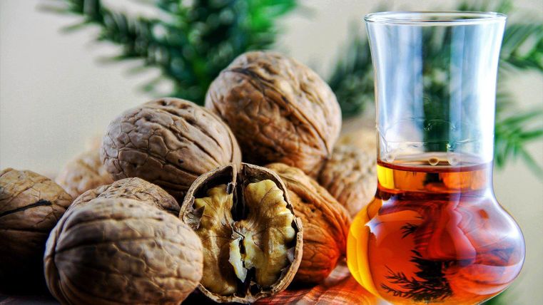 Eine Glas mit dunklem Getränk steht neben einer Gruppe von Walnüssen. Im Hintergrund sind grüne Blätter sichtbar.