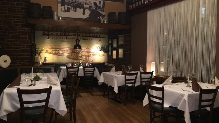 A cozy restaurant with elegant tables and chairs. The walls are decorated with pictures and wine bottles.