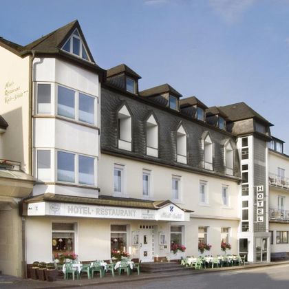 Een charmant hotel met restaurant, dat een uitnodigende gevel en grote ramen heeft. Er zijn zitgelegenheden buiten en een rustige omgeving.