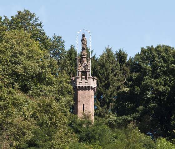 Die Mariens&auml;ule in Kyllburg ragt aus dichtem Wald hervor. Eine Statue steht auf einem steinernen Turm, umgeben von gr&uuml;nen B&auml;umen und blauem Himmel., &copy; TI Bitburger Land